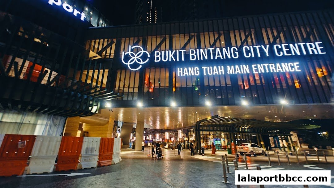 The illuminated entrance of Bukit Bintang City Centre at night, with people and cars.