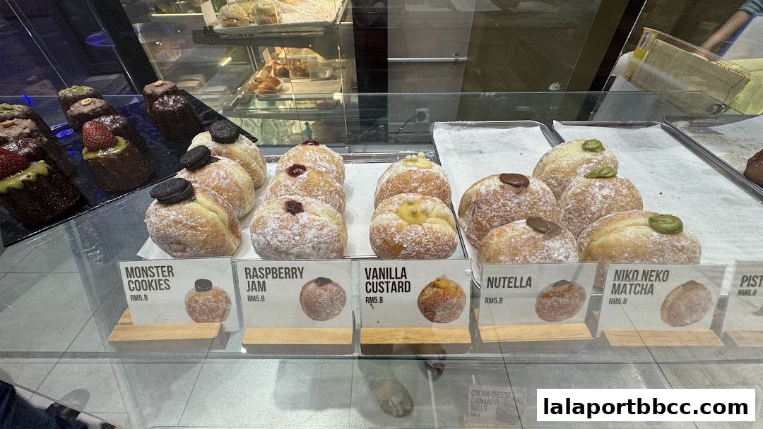 A display case filled with various donuts and pastries, each with a label indicating its flavor and price.