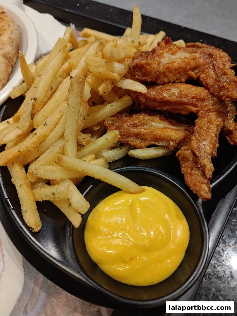 A plate of crispy fried chicken wings and french fries with a side of dipping sauce.