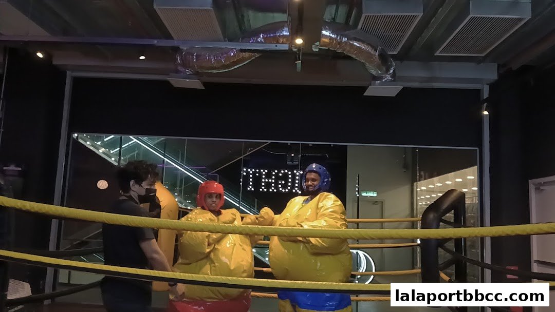 Two people in sumo suits inside a boxing ring with a referee.
