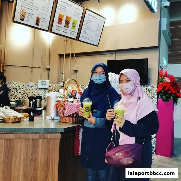 Two women in hijabs holding iced drinks in front of a counter with menus.