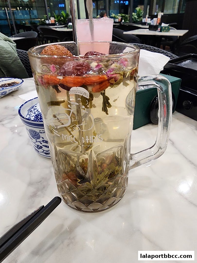 A large glass mug filled with herbal tea and dried fruits, with a pink drink in the background.