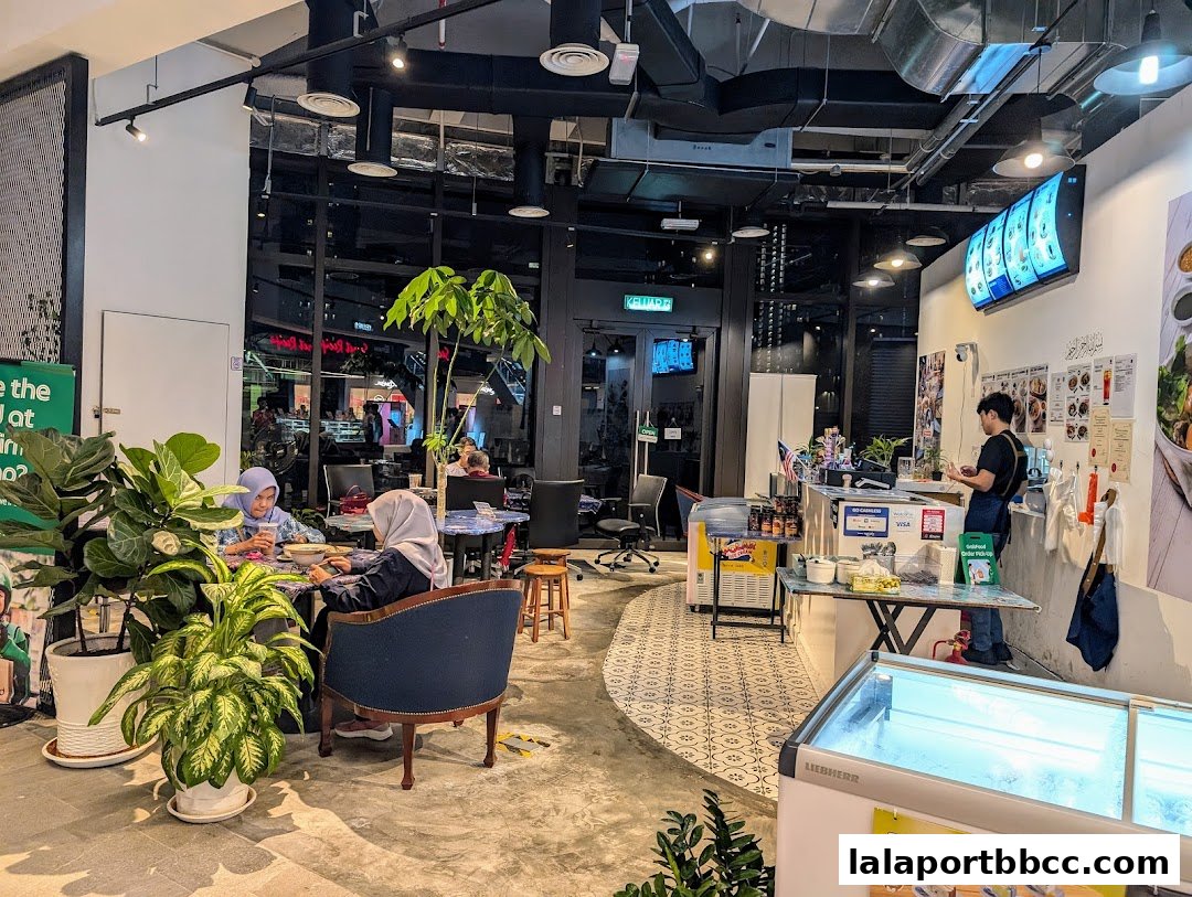 Interior of a modern cafe with customers dining and a staff member at the counter.