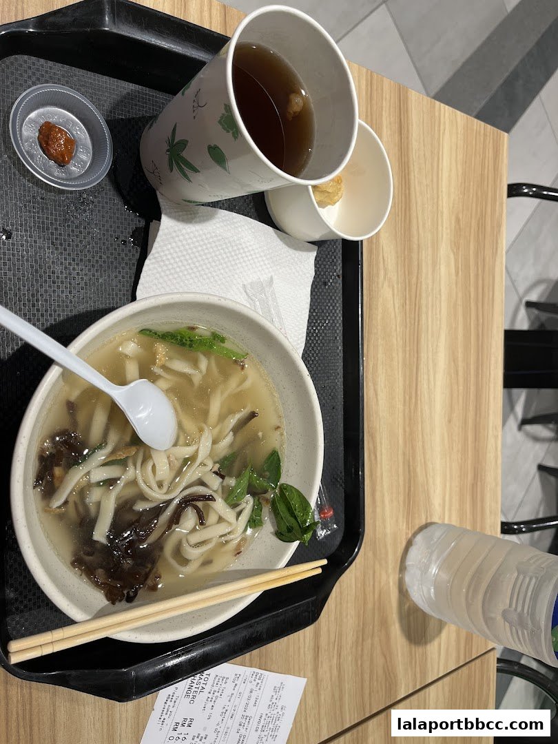 A bowl of noodles with broth, chopsticks, a cup of tea, and a bottle of water on a tray.