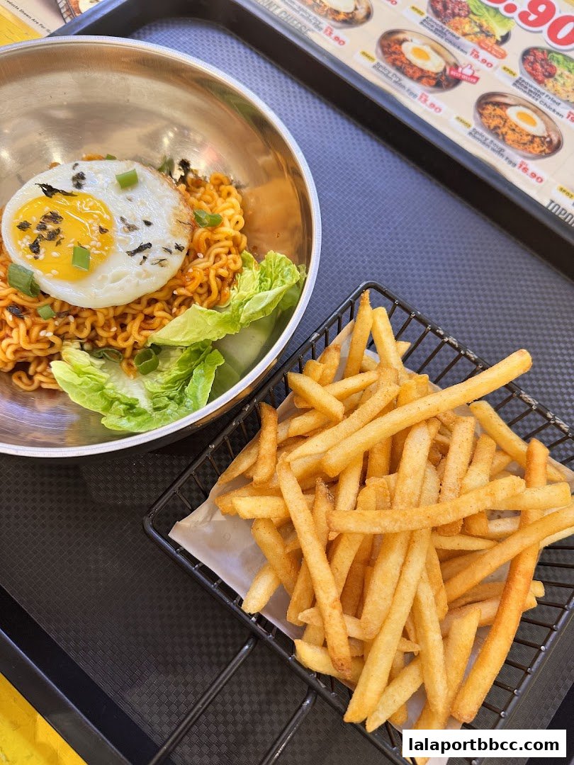 A close-up of Korean instant noodles with a fried egg and a side of french fries.
