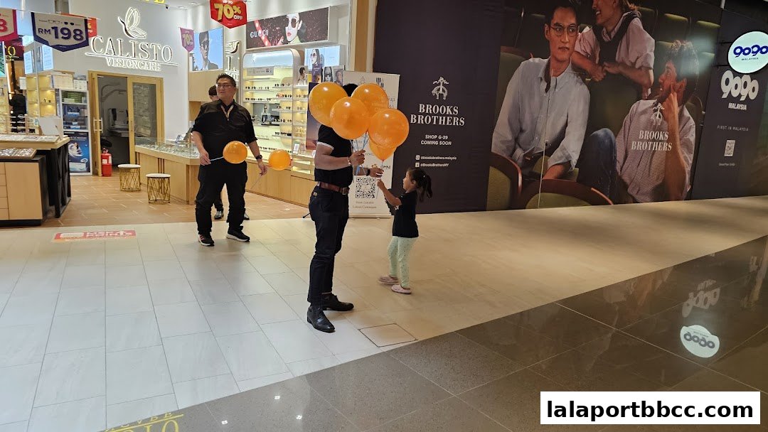 A man holds orange balloons while a child reaches for them in front of a shop.