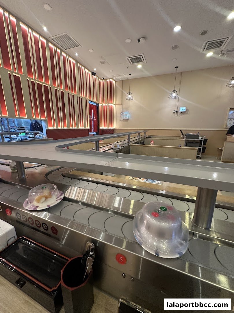Interior of a sushi restaurant with a conveyor belt featuring sushi dishes.