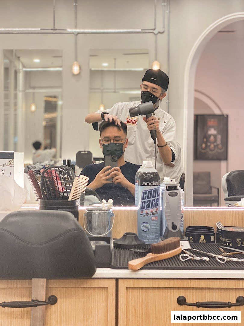 A barber is drying a customer's hair with a hairdryer inside a barbershop.