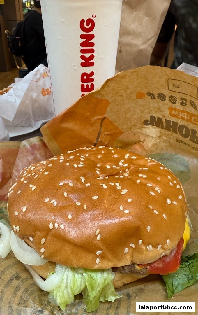 A close-up shot of a Burger King Whopper with a drink and packaging.