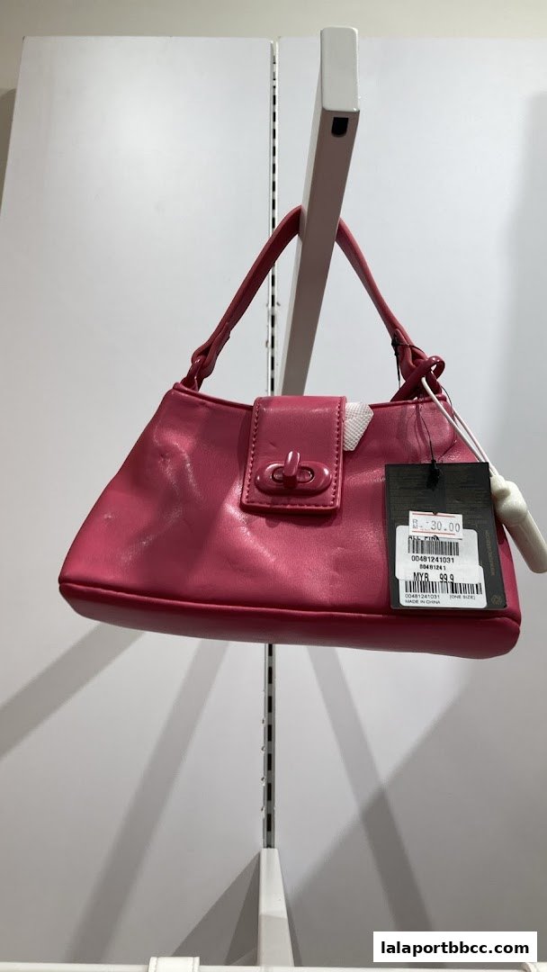 A bright pink shoulder bag with a clasp closure is displayed on a white shelf.