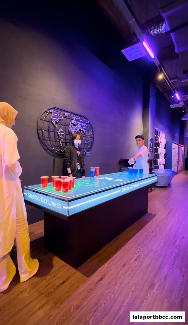 People playing a digital beer pong game with red and blue cups on a glowing table.