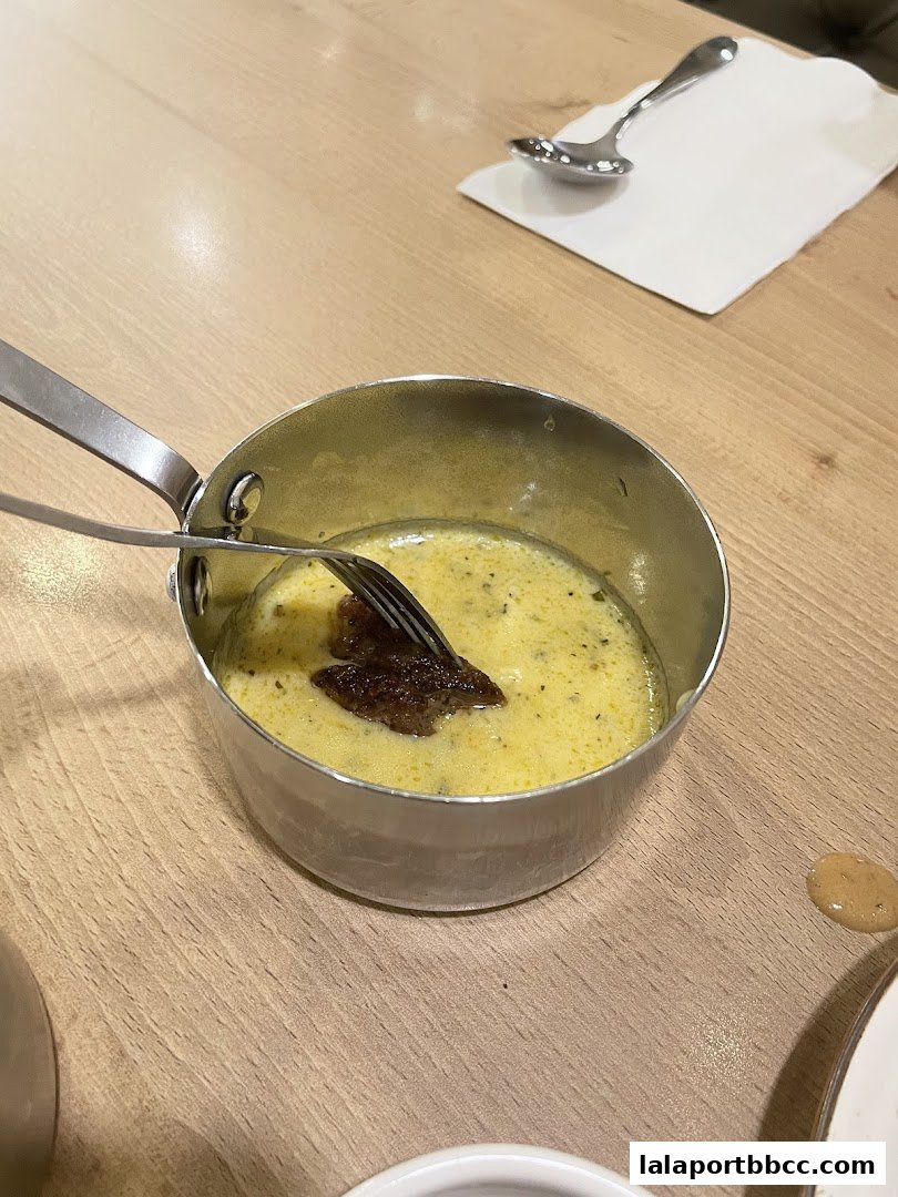 A fork is used to pick up a piece of meat from a creamy sauce in a metal pot.