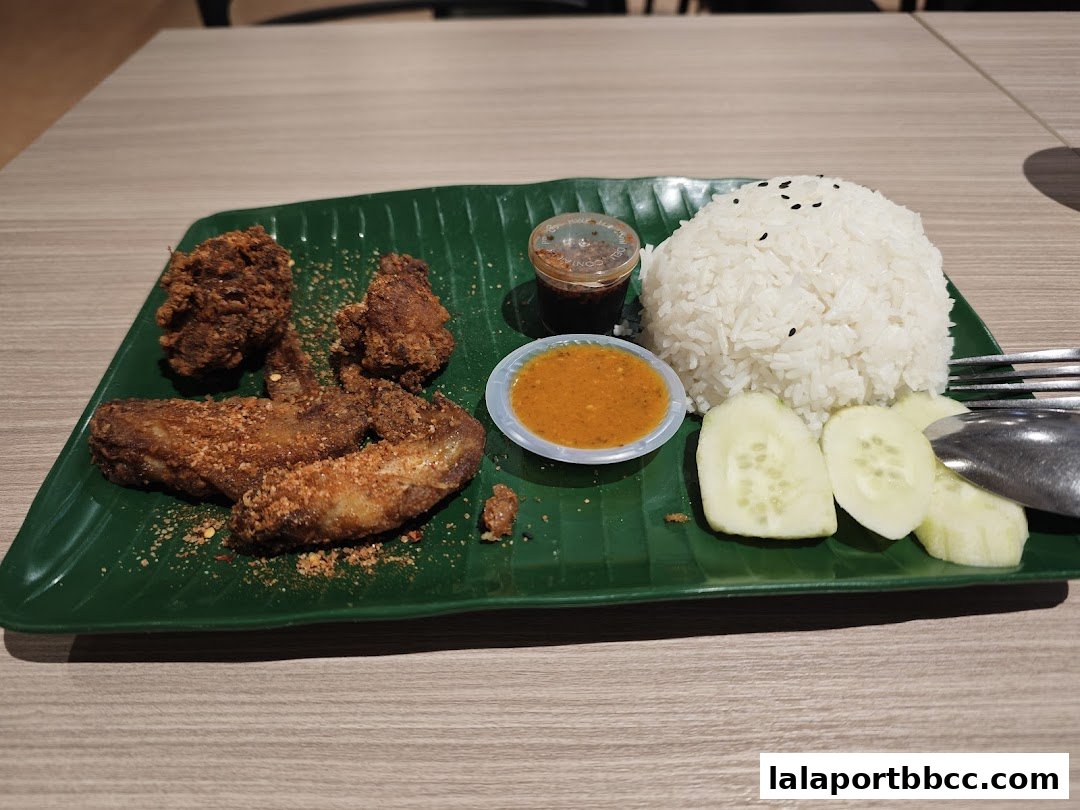 A plate of fried chicken wings with rice, cucumber slices, and dipping sauces.
