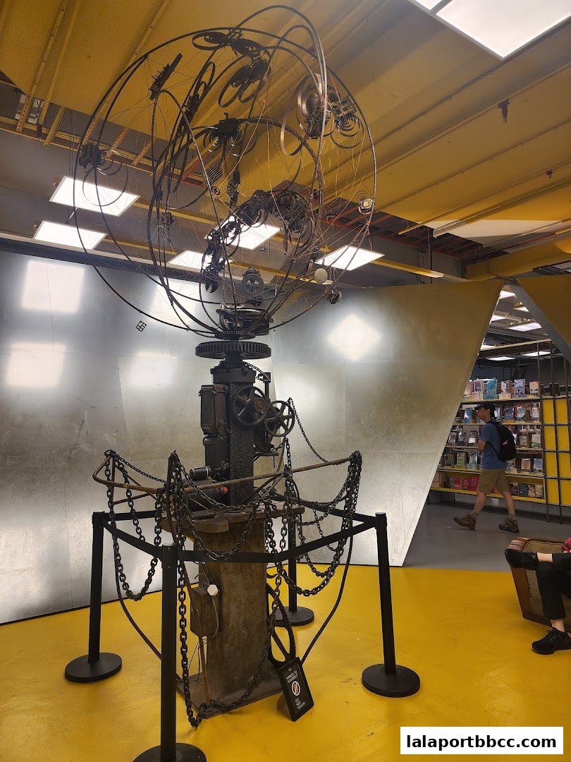 A large, intricate metal sculpture with chains in the center of a brightly lit room.