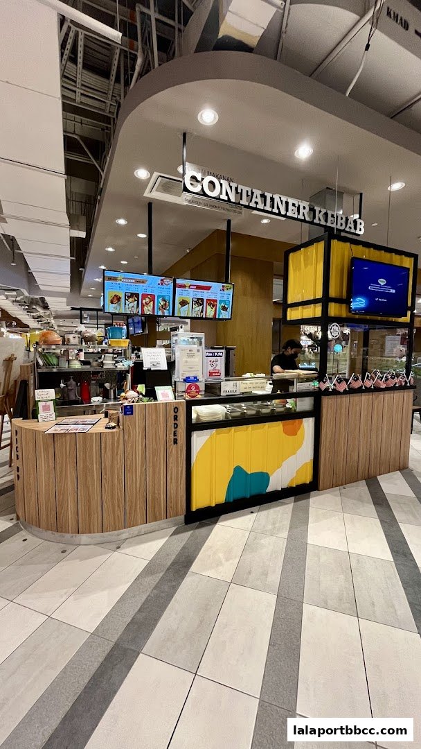 The Container Kebab shop counter with digital menus displaying food items and a staff member preparing orders.
