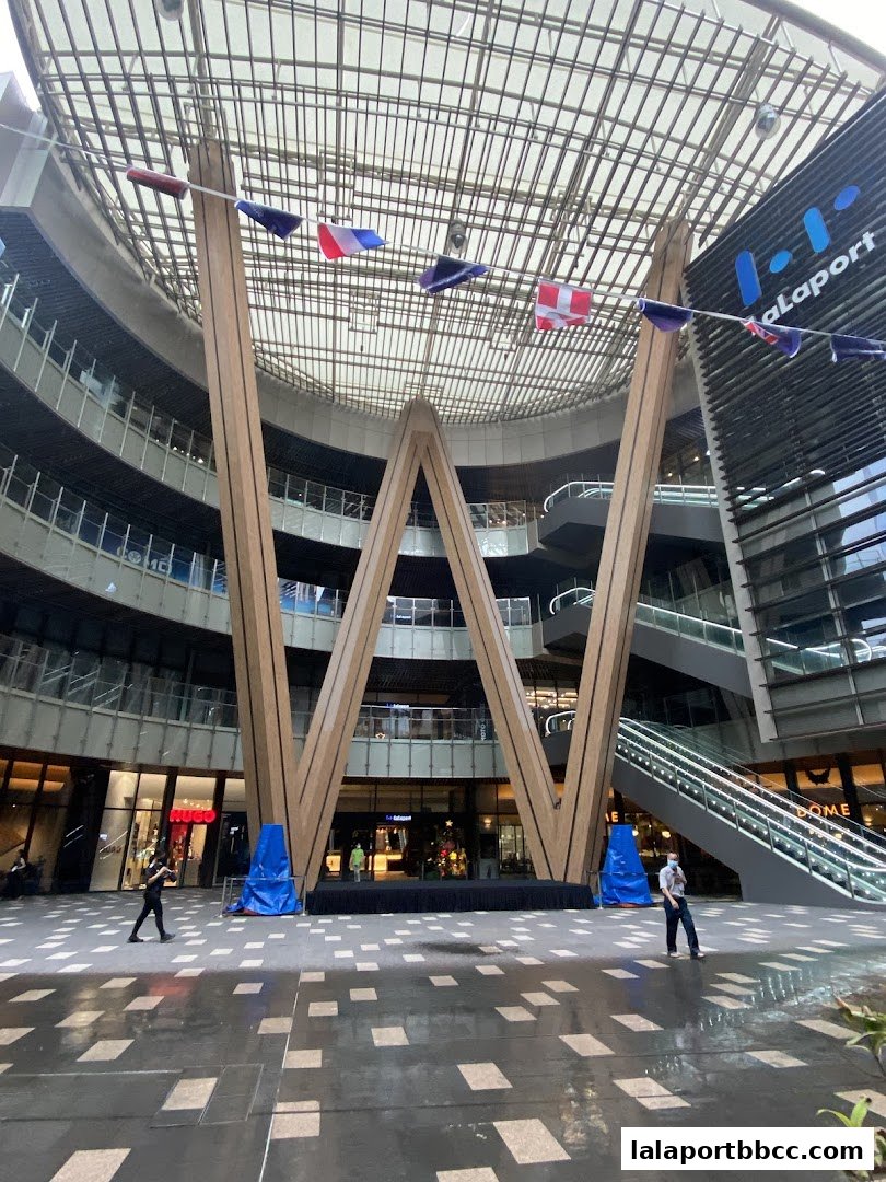 The south entrance of WOW Plaza features a large 'W' structure and international flags under a glass roof.