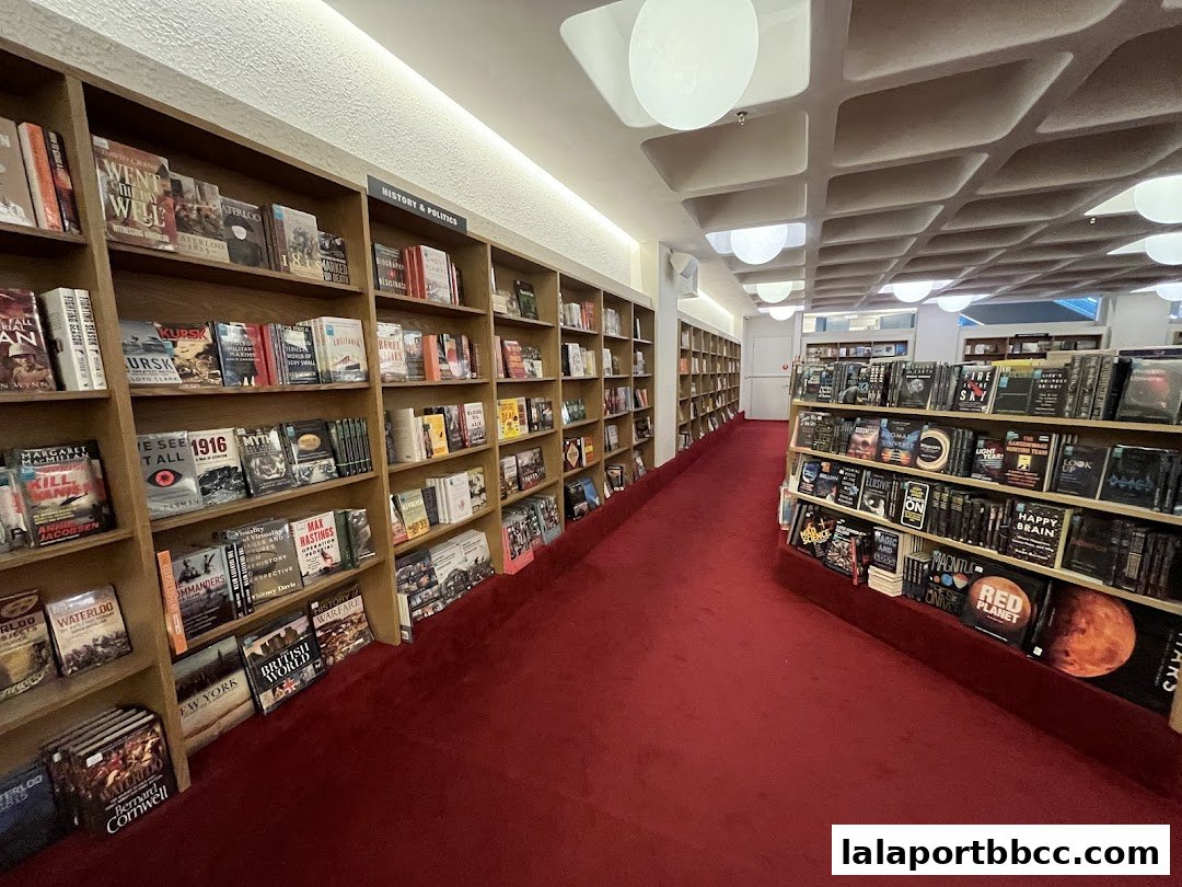 A wide aisle of bookshelves filled with books in a bookstore with a red carpet.