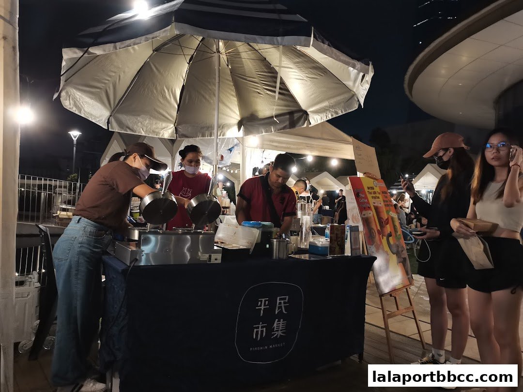 People working at a coffee stall at night, with customers looking at the menu.