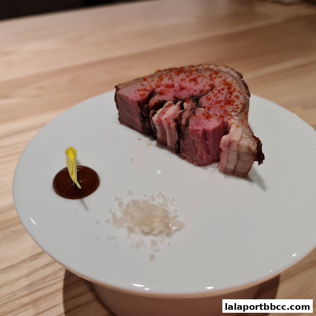 A slice of perfectly cooked meat with seasoning, sauce, and salt on a white plate.