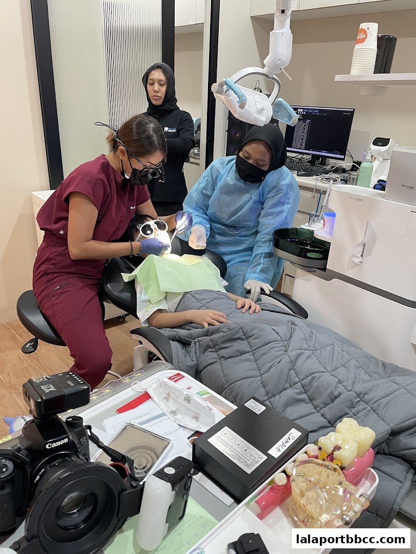 Dental professionals attend to a patient in a modern clinic, with dental equipment and models visible.