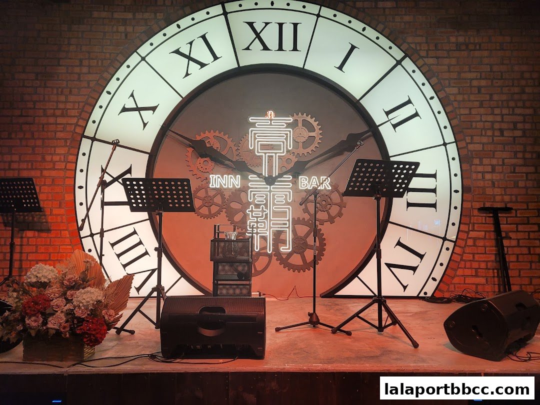 A stage setup with a large clock backdrop, microphones, speakers, and floral decorations.