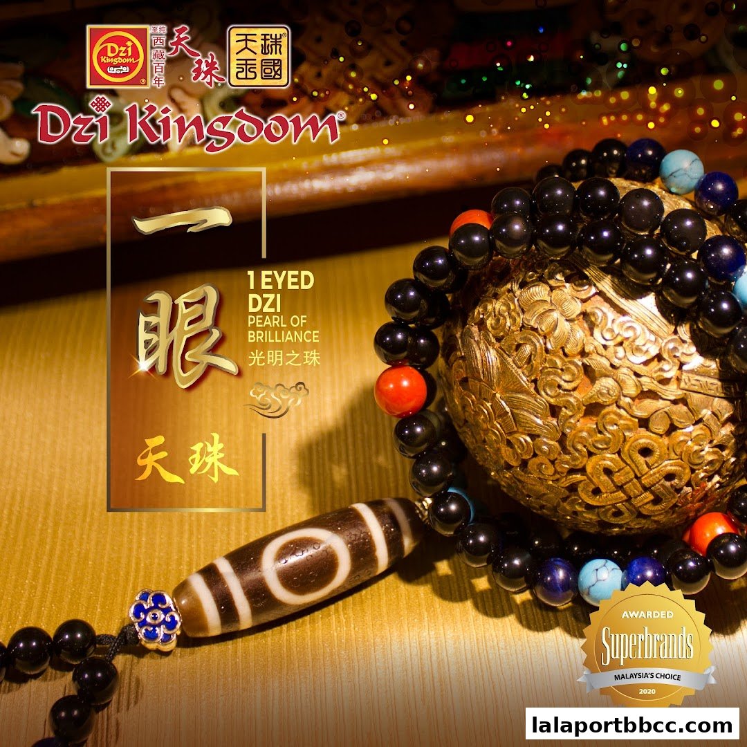 A close-up of a Dzi bead bracelet with a golden ornate sphere and the shop's branding.