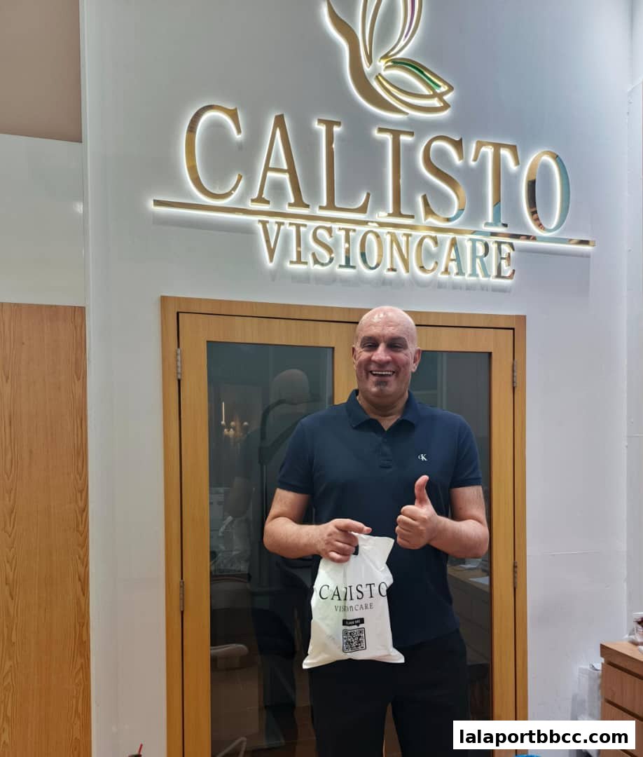 A man stands in front of the Calisto Visioncare sign, holding a branded bag and giving a thumbs up.