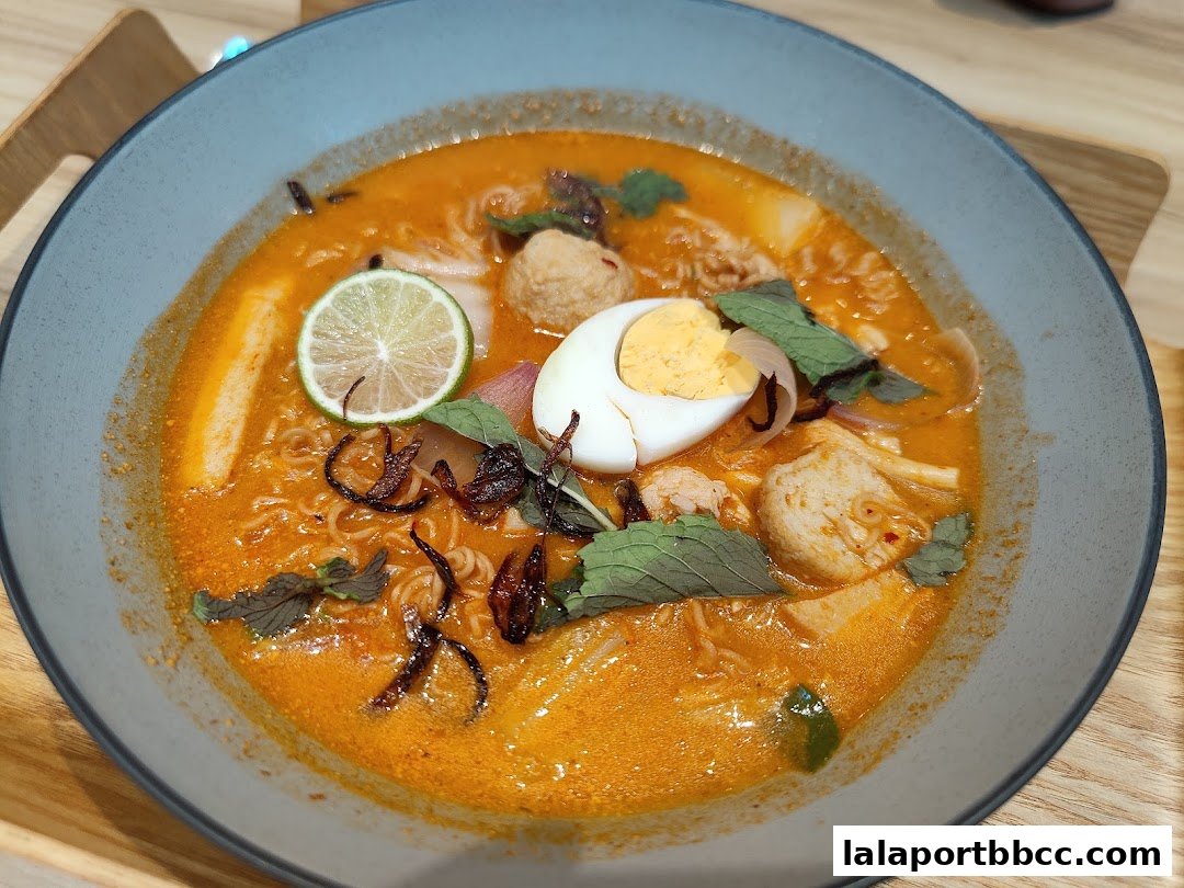 A close-up shot of a delicious bowl of Laksa with egg, lime, and herbs.