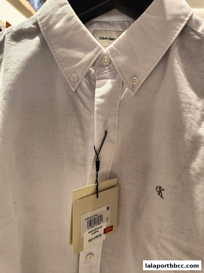 Close-up of a white Calvin Klein button-down shirt with a tag showing price and discount.