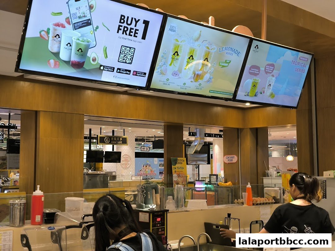 Digital menu boards display drinks and promotions above a beverage counter with staff.