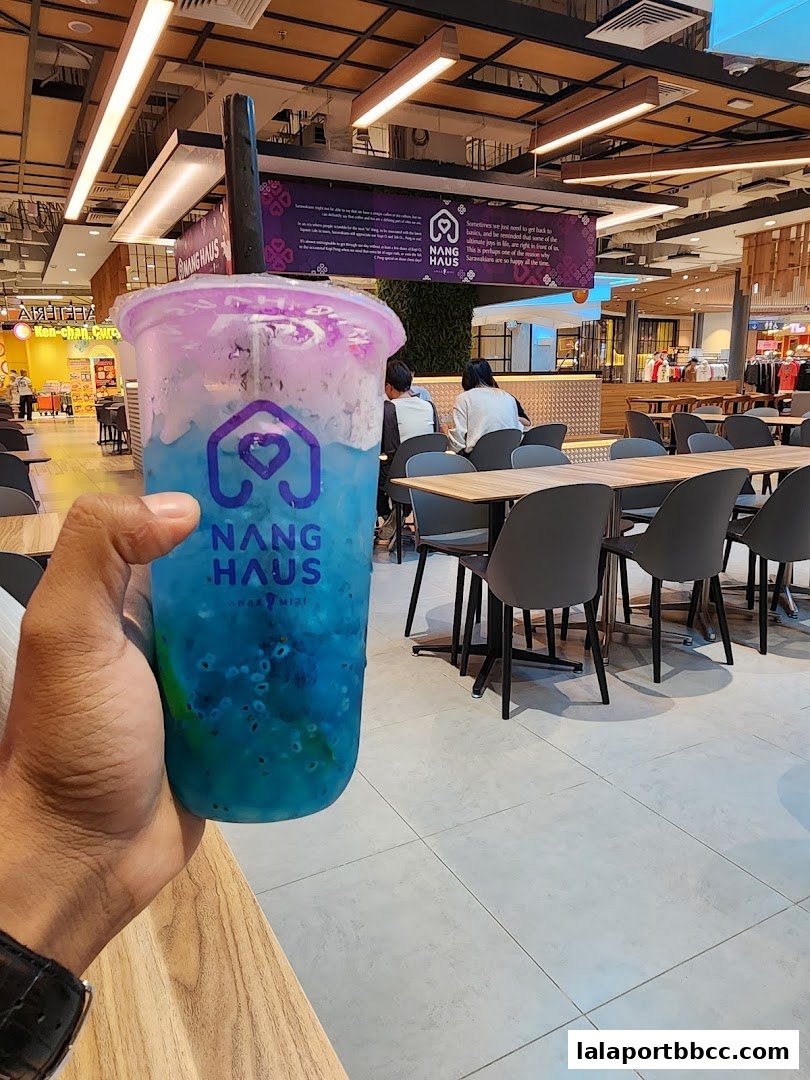A hand holds a colorful blue and purple drink with the Nang Haus logo in a modern cafe setting.