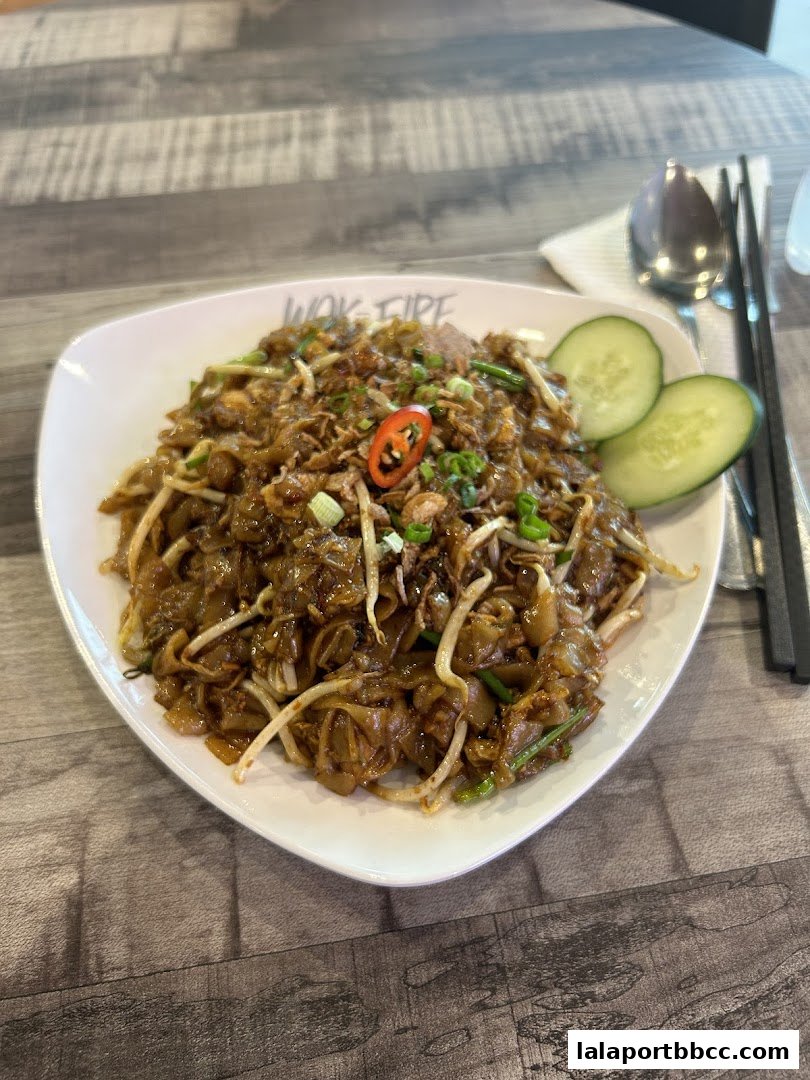 A plate of delicious stir-fried noodles with cucumber slices and chili garnish.
