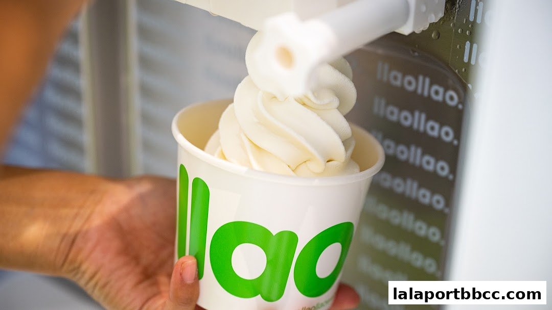 A hand holds a cup of creamy frozen yogurt being dispensed from a machine.