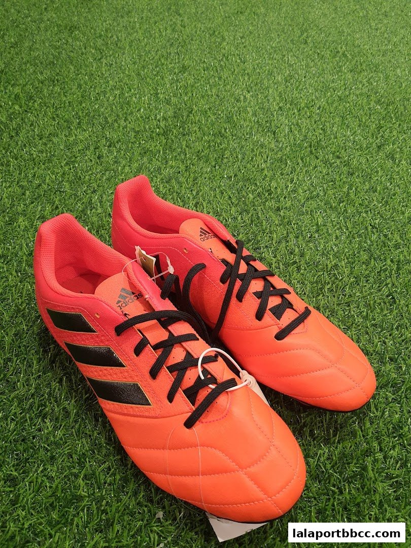 A pair of bright orange Adidas soccer cleats with black laces on a green grassy surface.