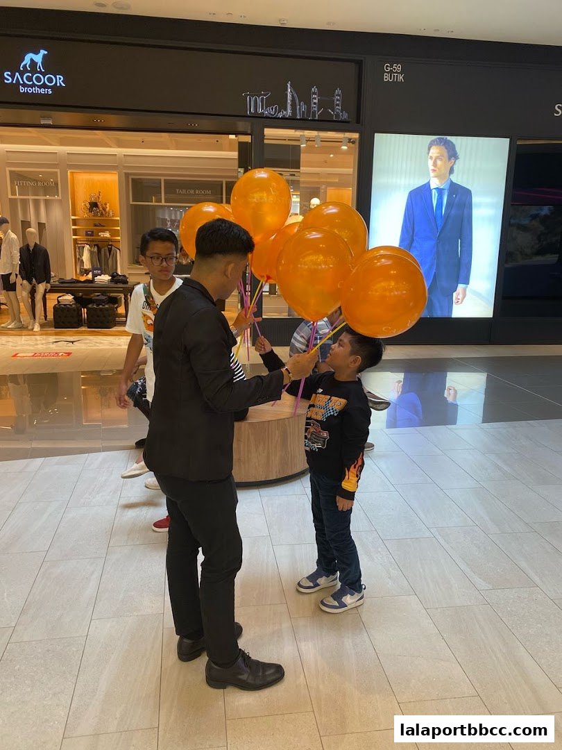 A man hands orange balloons to a child in front of a shop.
