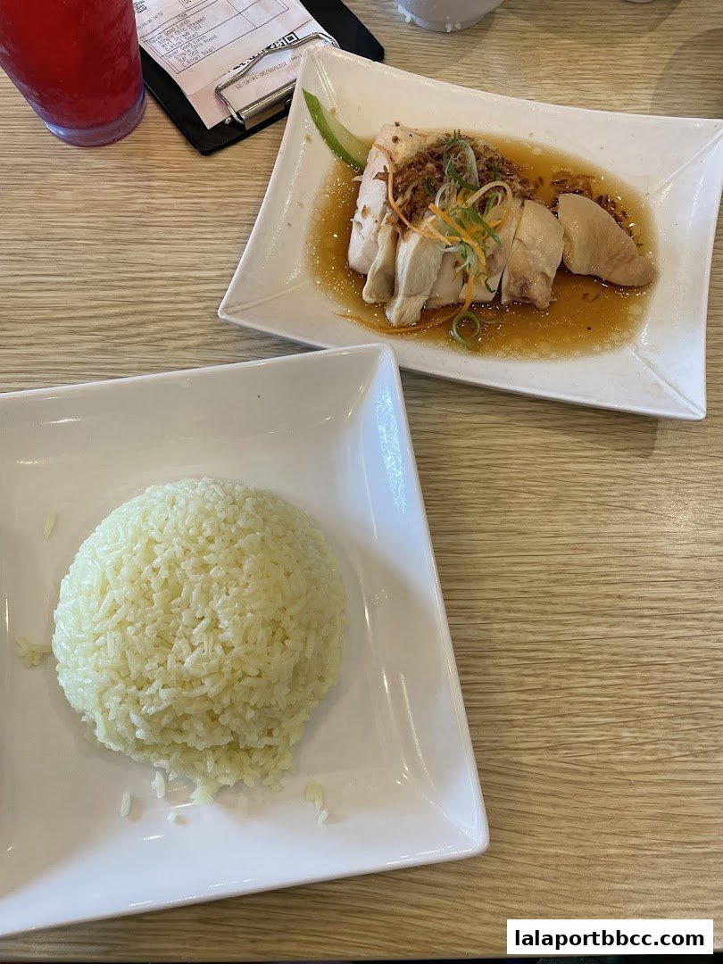 A plate of Hainanese chicken rice with a side of fragrant rice and a drink.