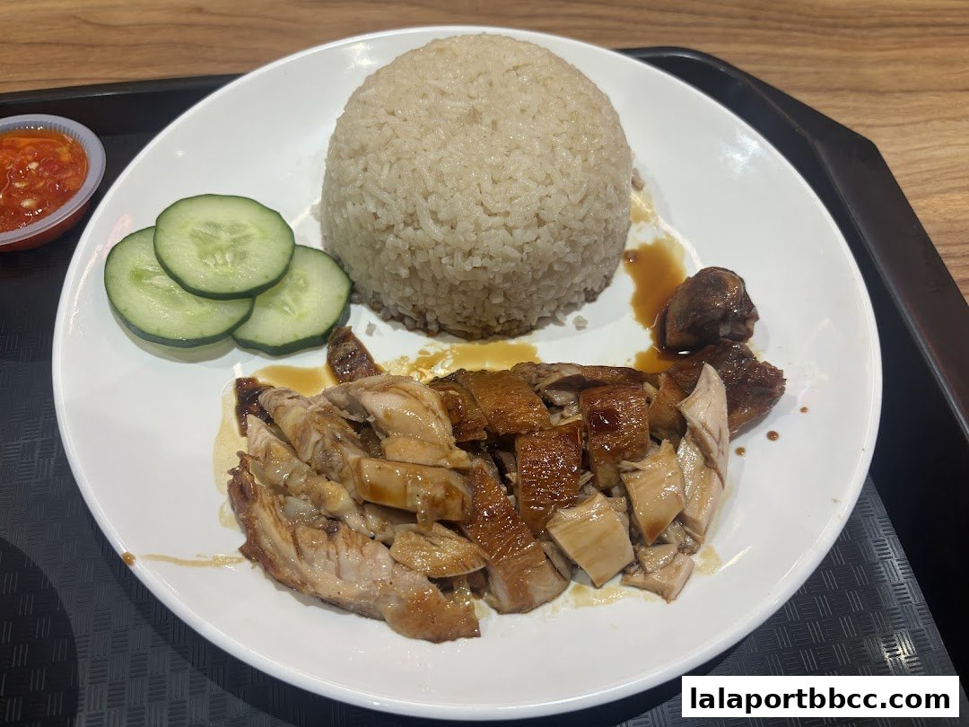 A plate of delicious chicken rice with sliced cucumbers and chili sauce.