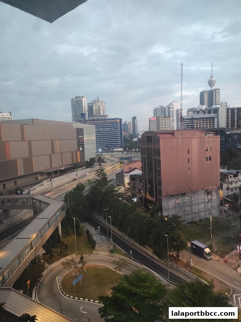 A cityscape view showing buildings, roads, and a sky bridge under a cloudy sky.
