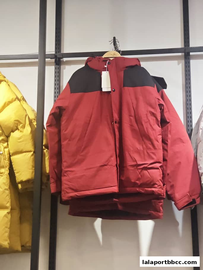 A red puffer jacket with black accents is displayed on a hanger, with a yellow jacket visible to the left.