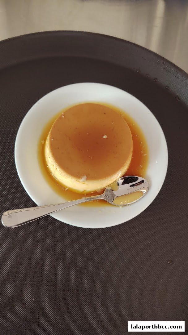 A close-up shot of a creamy caramel pudding served on a white plate with a spoon.