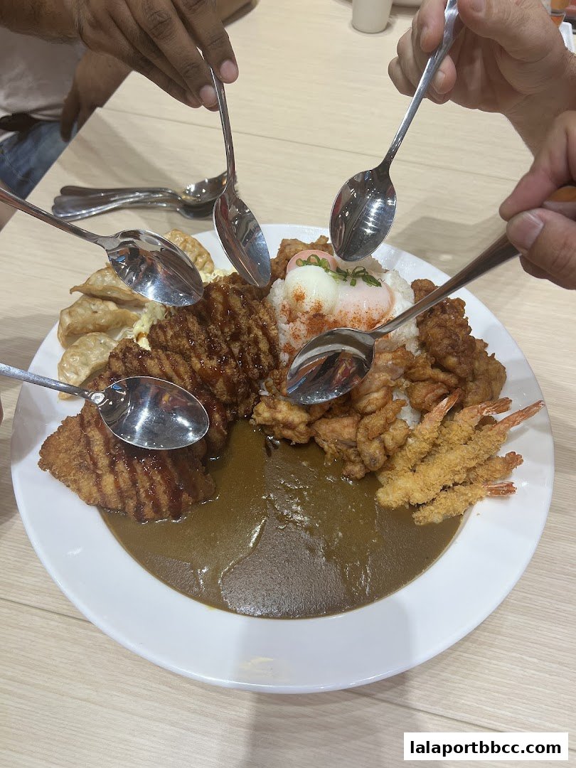 A large plate of Japanese curry with various toppings and multiple spoons ready to eat.
