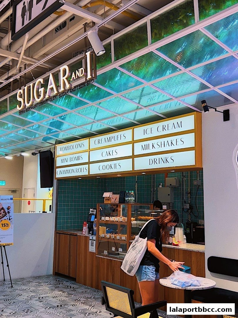 A customer at the Sugar and I dessert shop, with a menu board displaying various sweet treats.