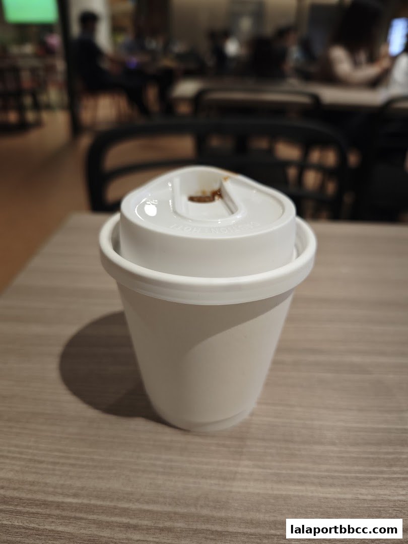 A white disposable coffee cup with a lid sits on a wooden table.
