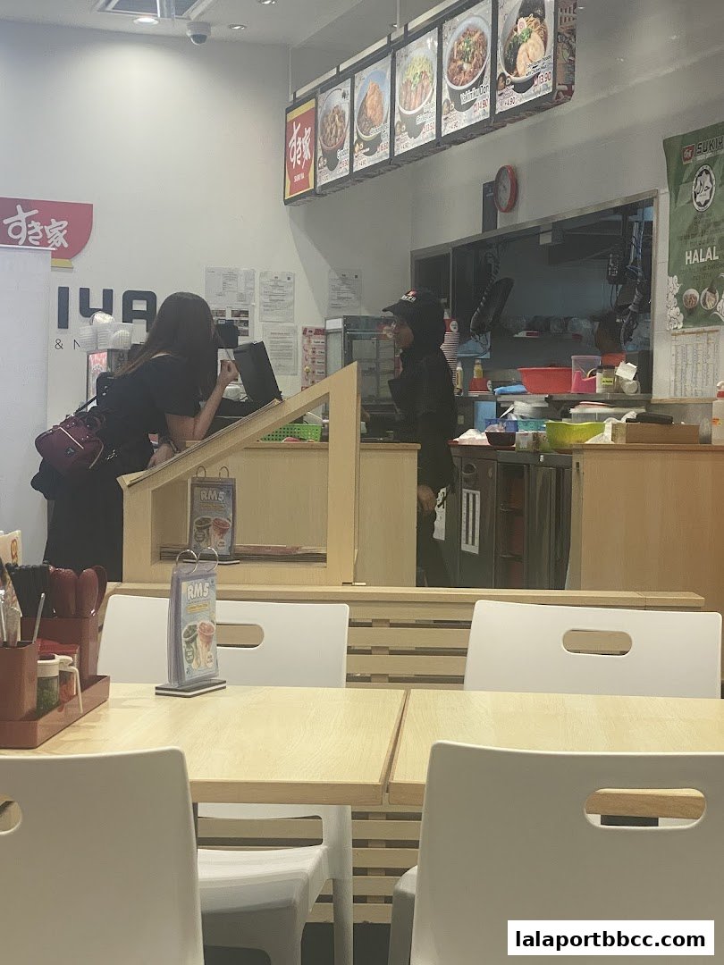 Customers ordering at the counter of a Sukiya restaurant with menu displays above.