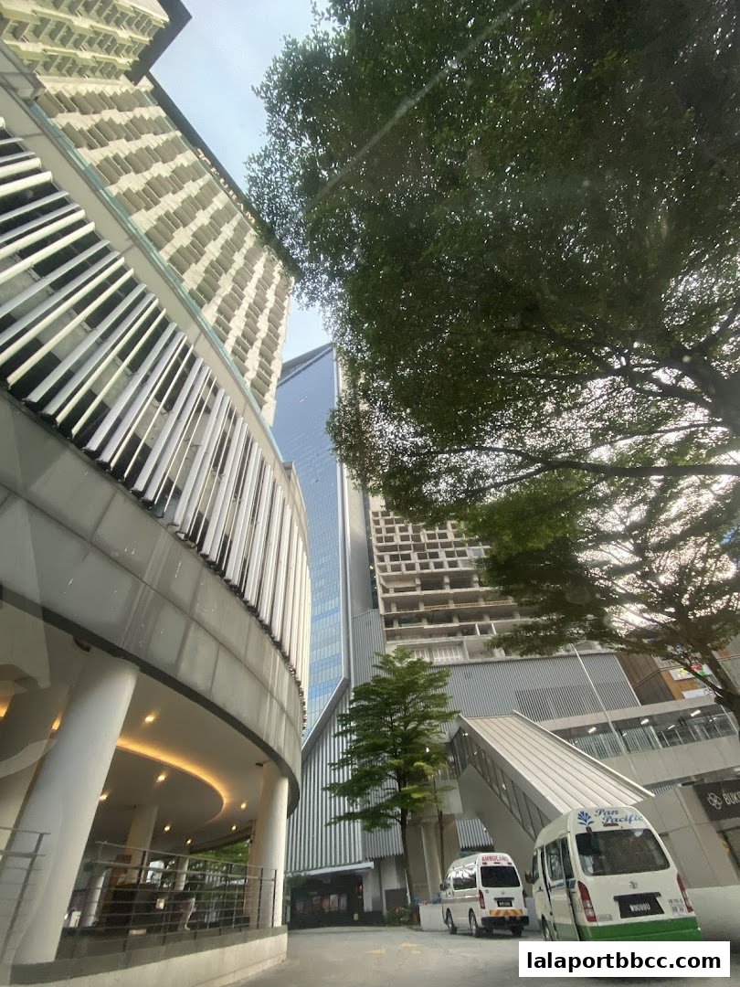 Modern architecture with a hotel entrance, trees, and vehicles on a street.