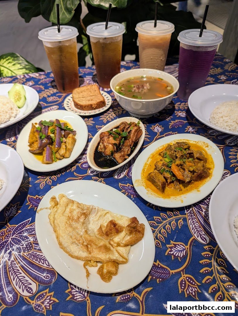 A table laden with various Malaysian dishes and drinks, set on a batik-patterned cloth.