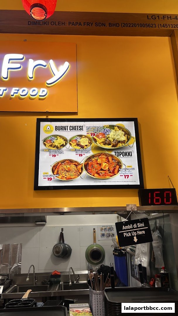 A digital menu board displaying various Korean fried chicken and topokki dishes at Papa Fry.