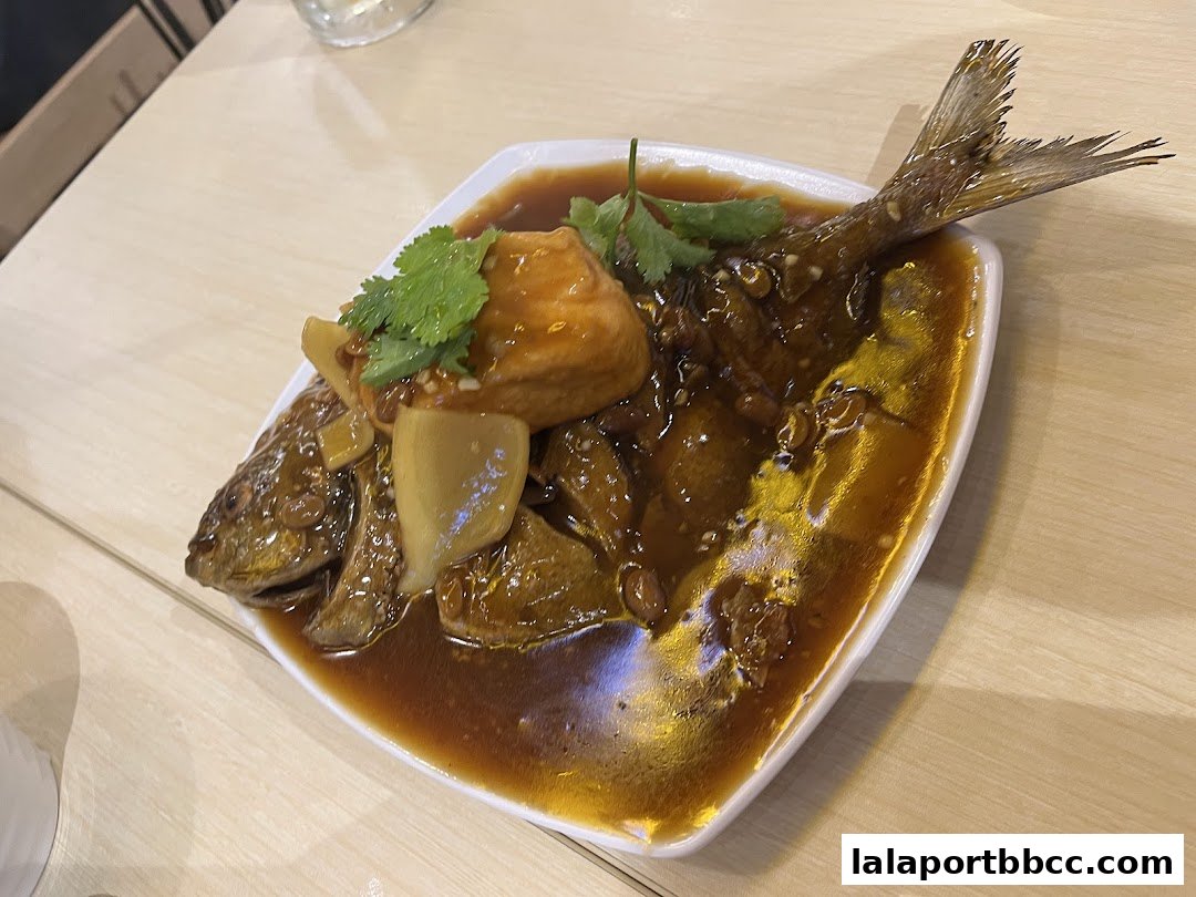 A whole fish dish with sauce, tofu, and cilantro on a white plate.