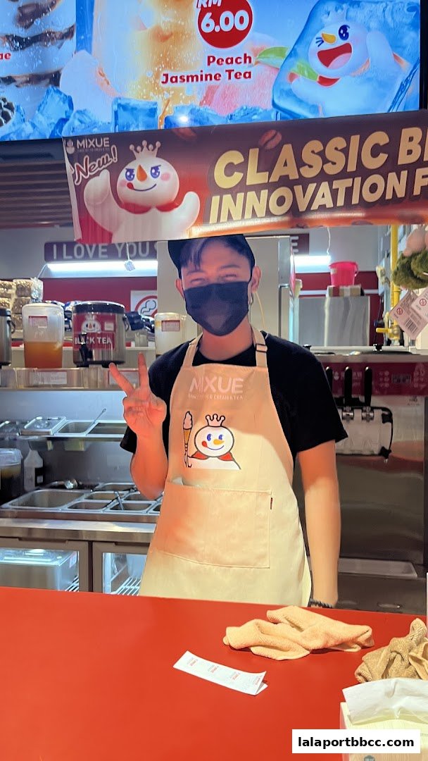 A smiling staff member at MIXUE LaLaport BBCC Bukit Bintang Kuala Lumpur, posing with a peace sign.
