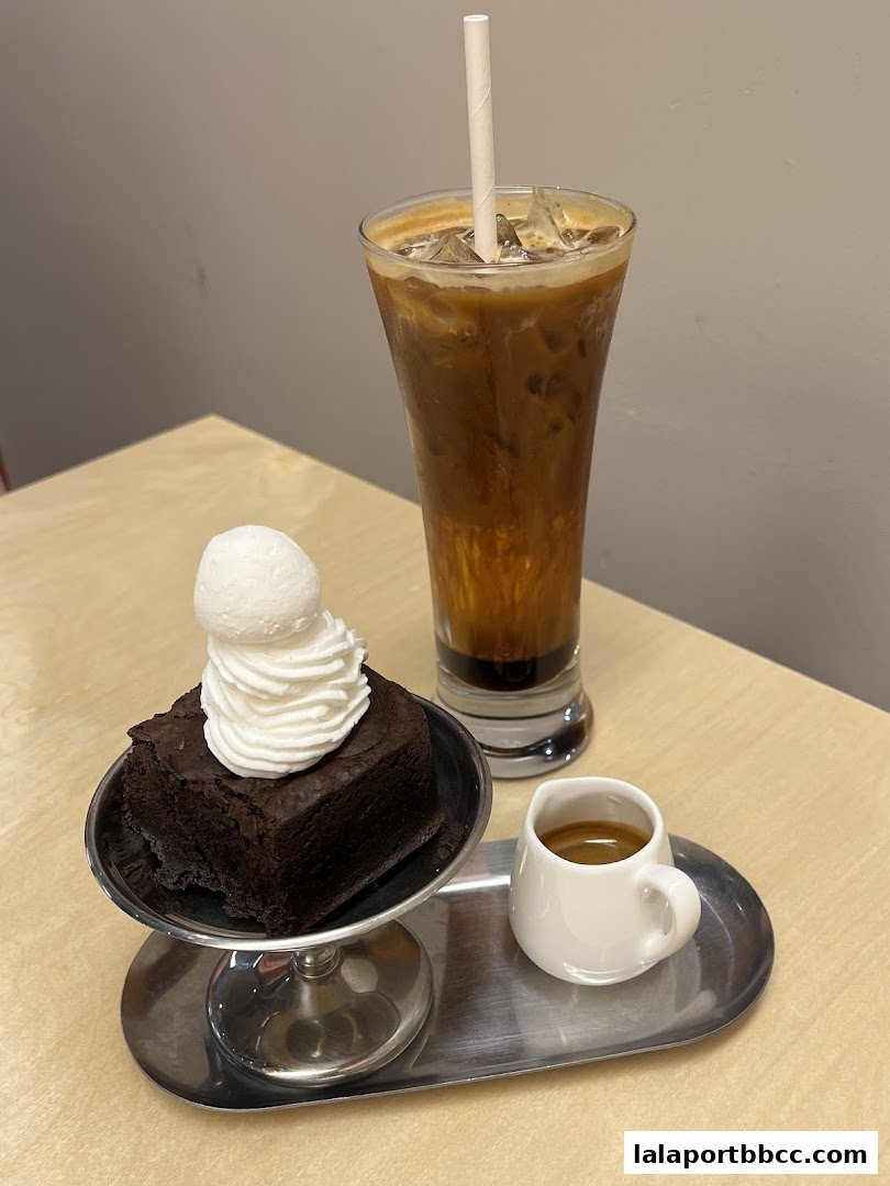 A rich chocolate brownie topped with whipped cream and a scoop of ice cream, served with iced coffee and espresso.